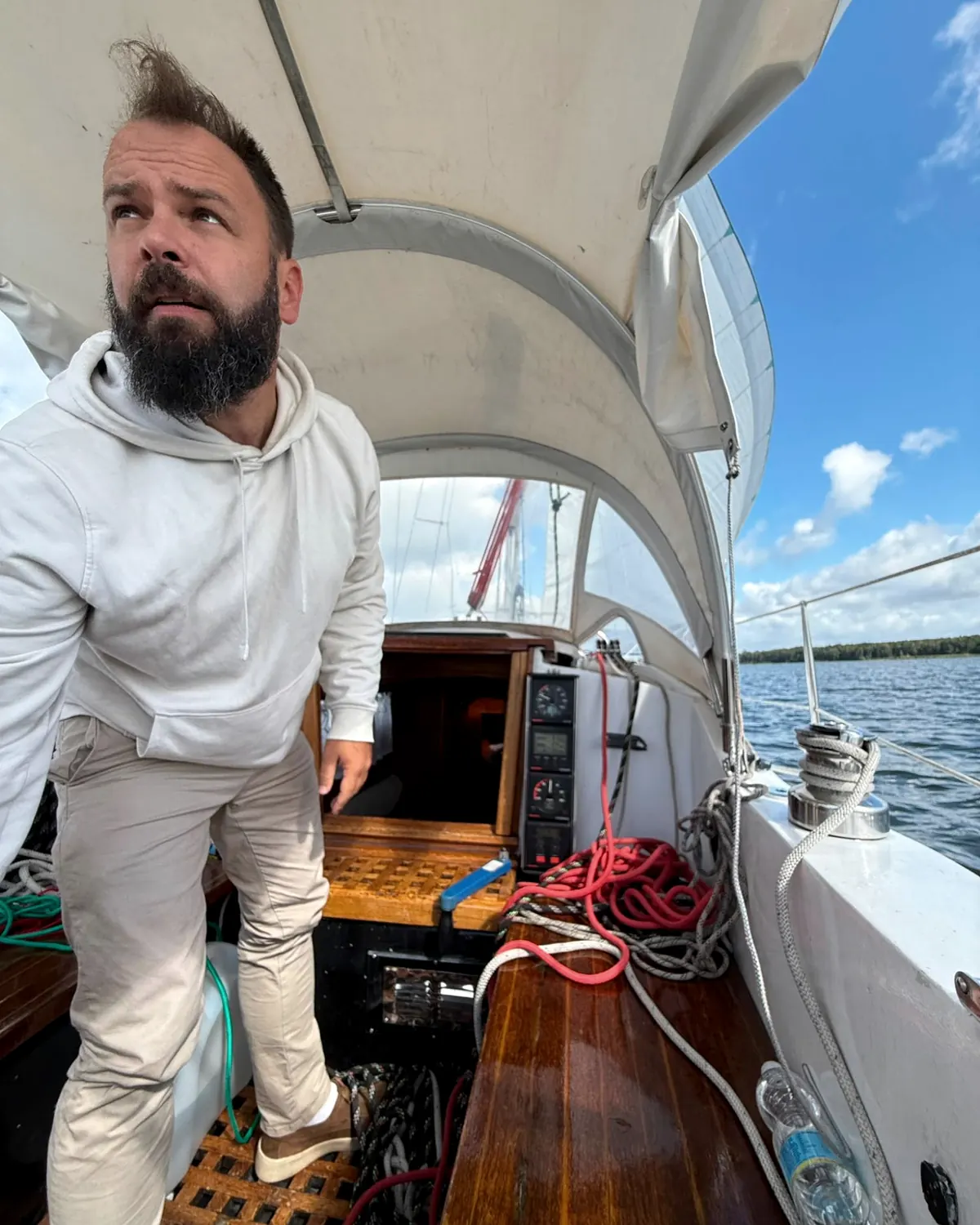Johannes steht im Wind unter dem Verdeck eines Segelboots, die Haare zerzaust, und blickt angespannt nach oben in die Takelage.